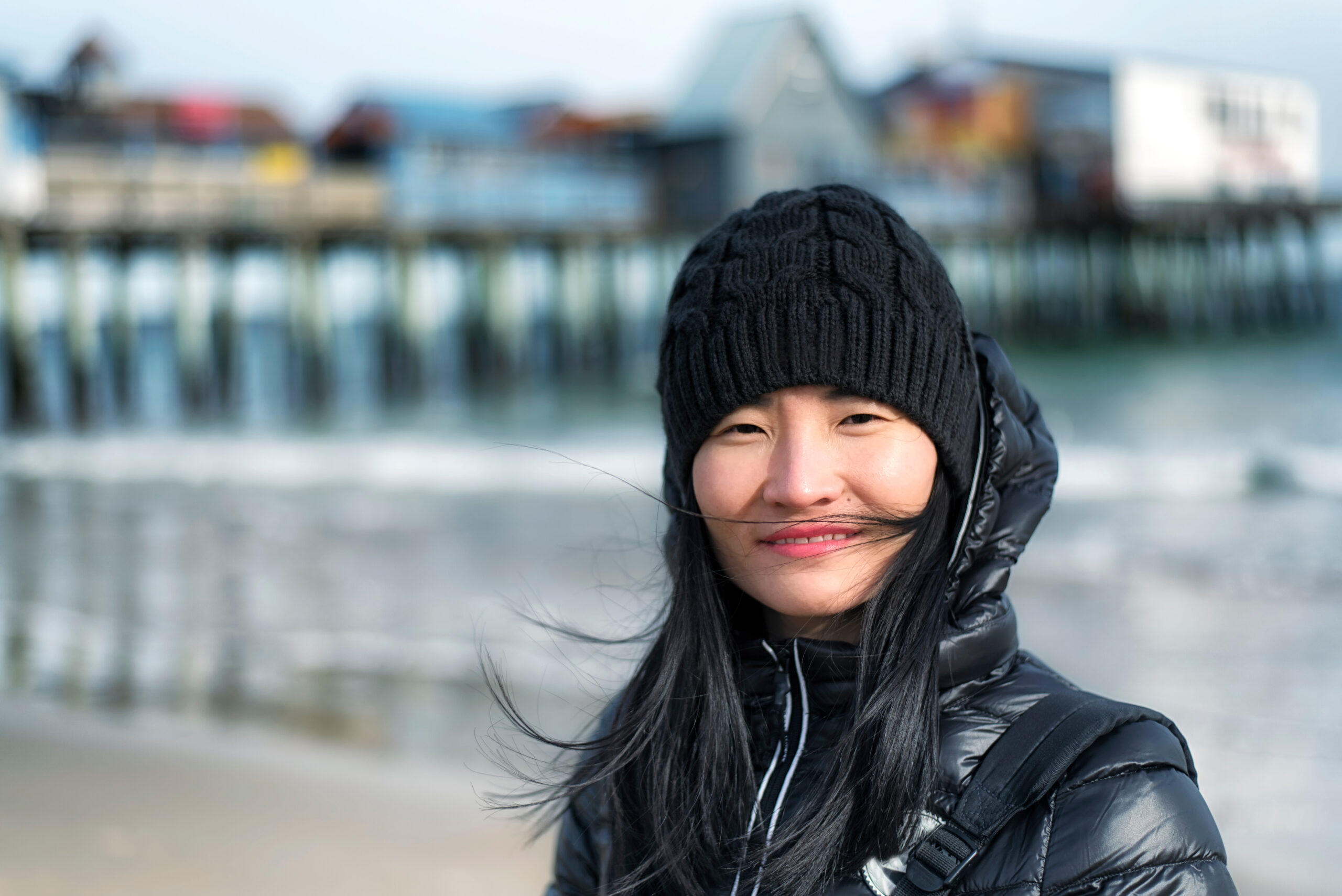 A chinese woman wearing a winter jacket in the blowing wind at Old Orchard Beach Maine on a sunny day.