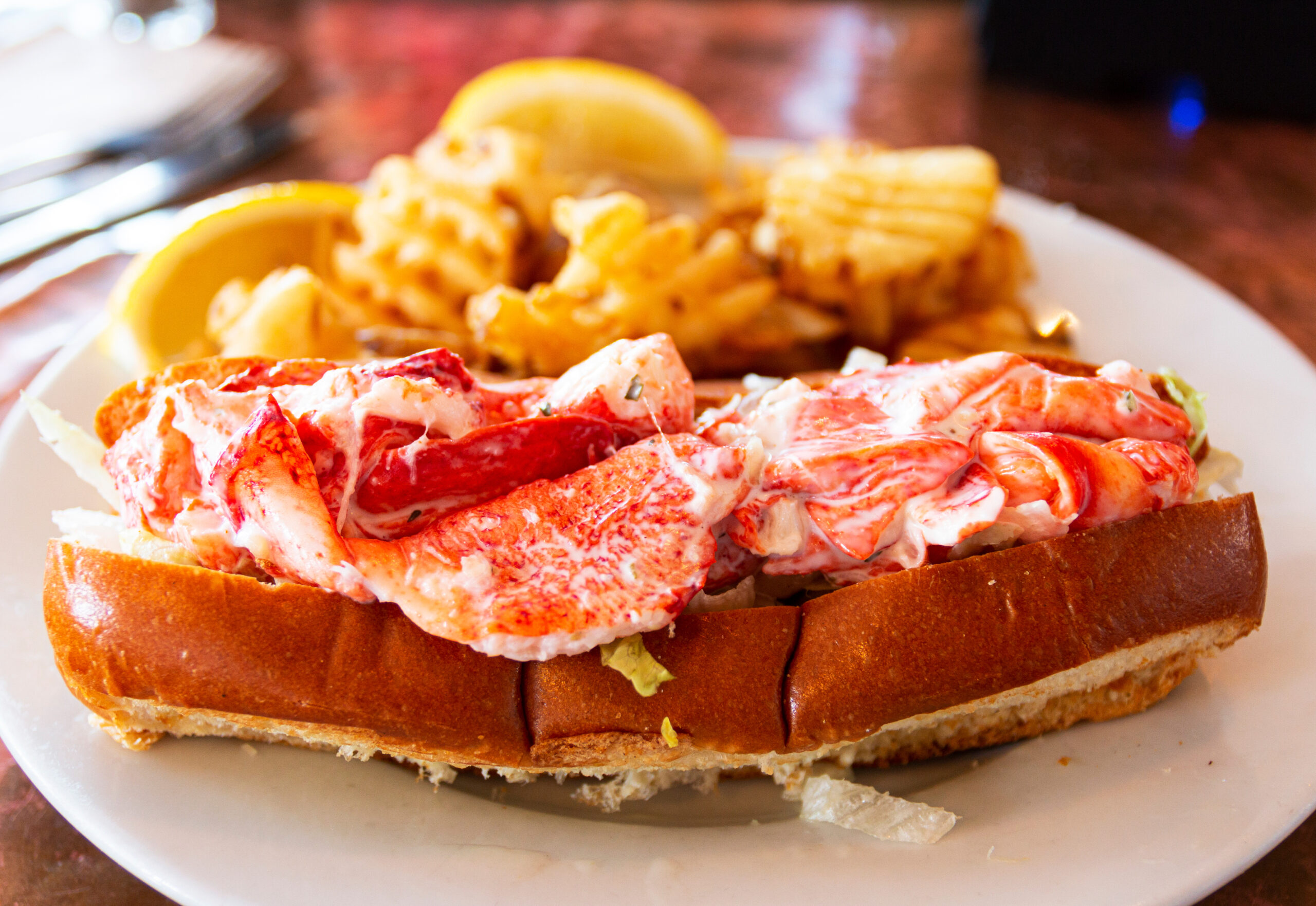 Lobster roll on a plate in a restaurant in Maine A fresh lobster roll served with waffle fries in a restaurant in Portland Maine.